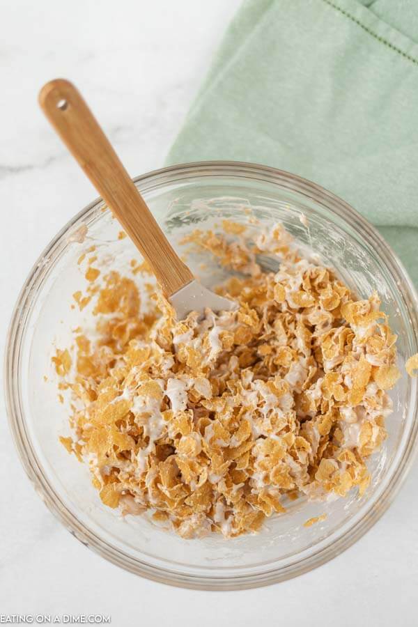 Close up image of cornflake bars being mixed in a glass bowl with a spatula. 