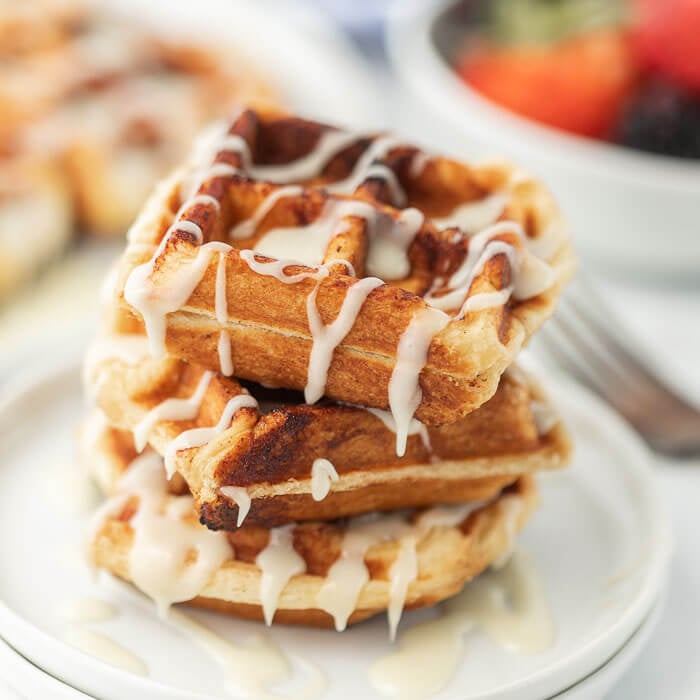Close up of cinnamon Roll Waffles stacked on top of each other with frosting drizzled on top.  