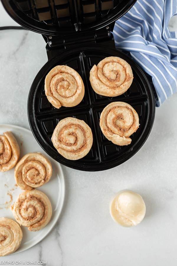The raw cinnamon rolls placed on top of the open waffle iron. 