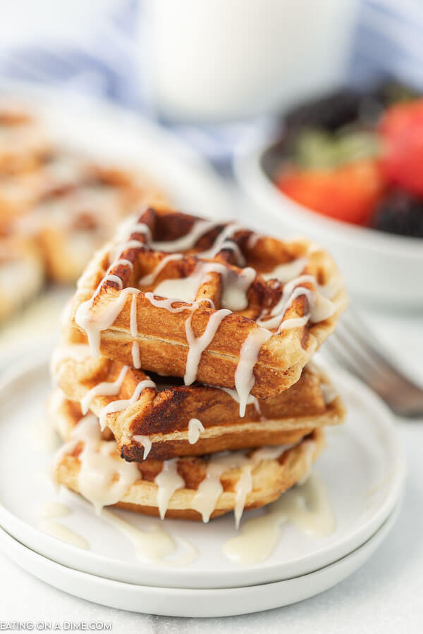 Cinnamon Roll Waffles stacked on top of each other with frosting drizzled on top.  