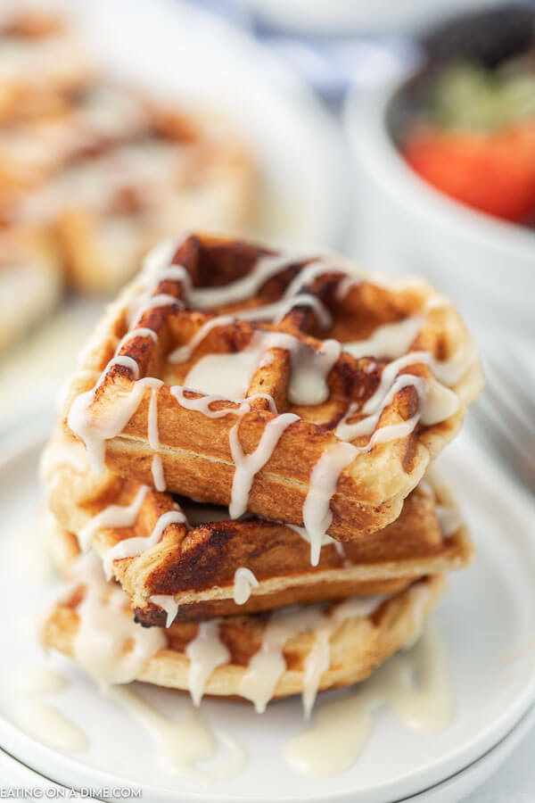 3 Cinnamon Roll Waffles stacked on top of each other with frosting drizzled on top.  