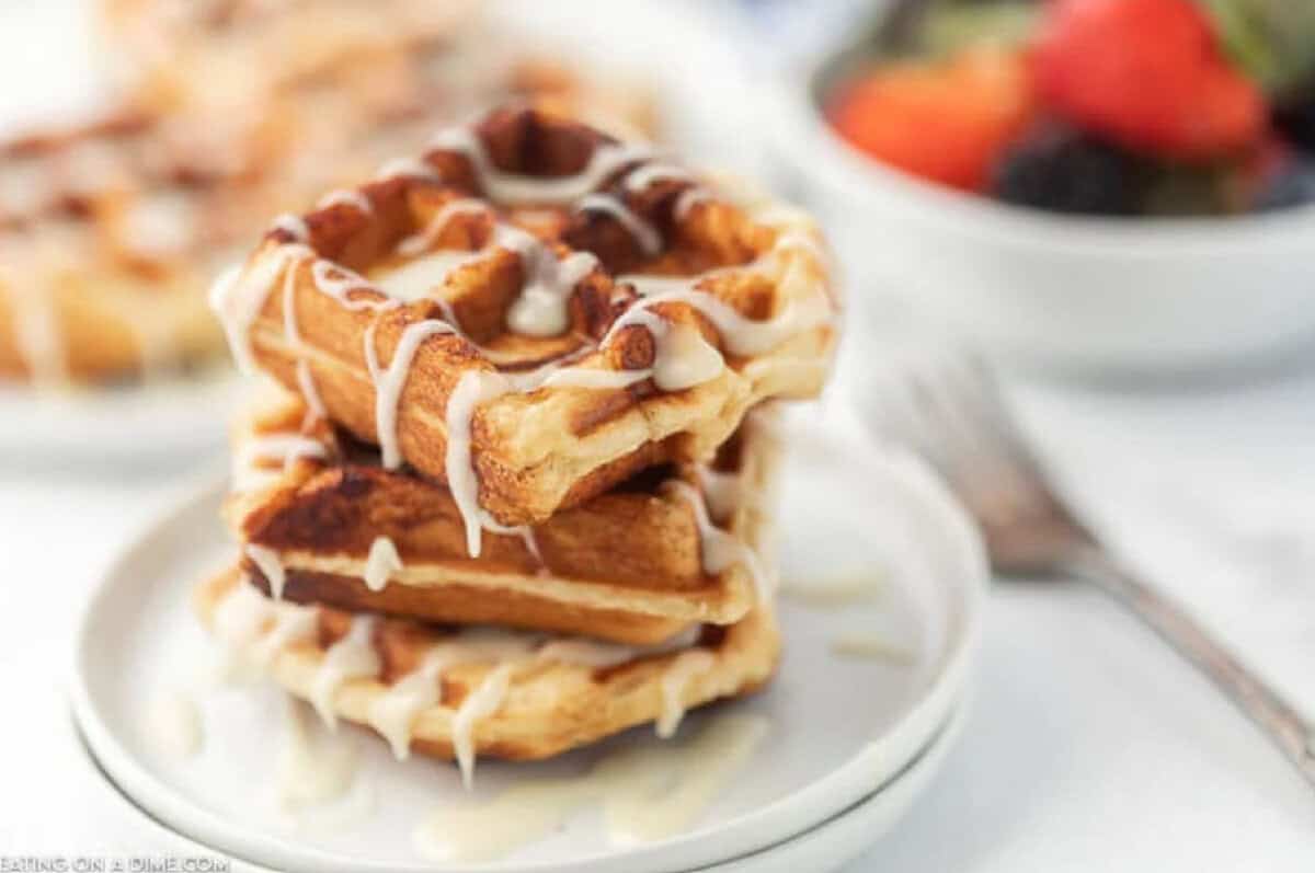 Learn how to make Cinnamon Roll Waffles. These cinnamon rolls in waffle maker are so easy! The icing just drizzles down the cinnamon bun waffles. Yum! Try these Cinnamon rolls in a waffle maker today. Your family will love them! Waffles stacked on top of each other with frosting drizzled on top.