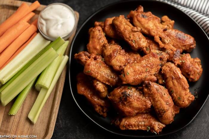 Platter of chicken wings beside cut up veggies and ranch dressing.