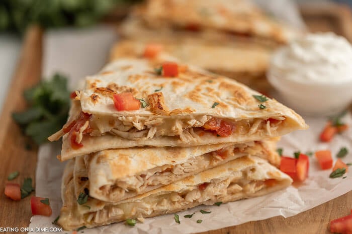 Close up image of chicken quesadilla's stacked with a side of sour cream. 