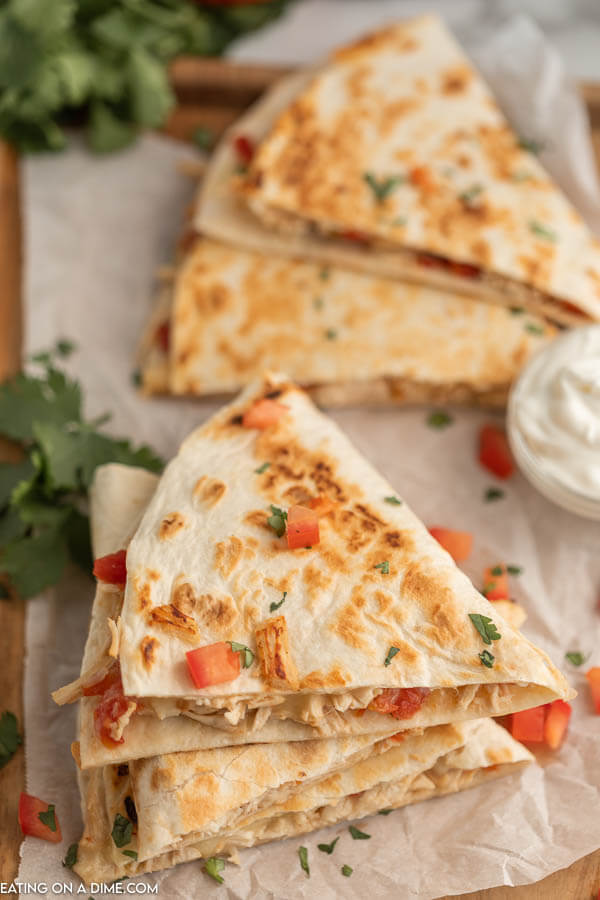 Close up image of chicken quesadilla's stacked with a side of sour cream. 