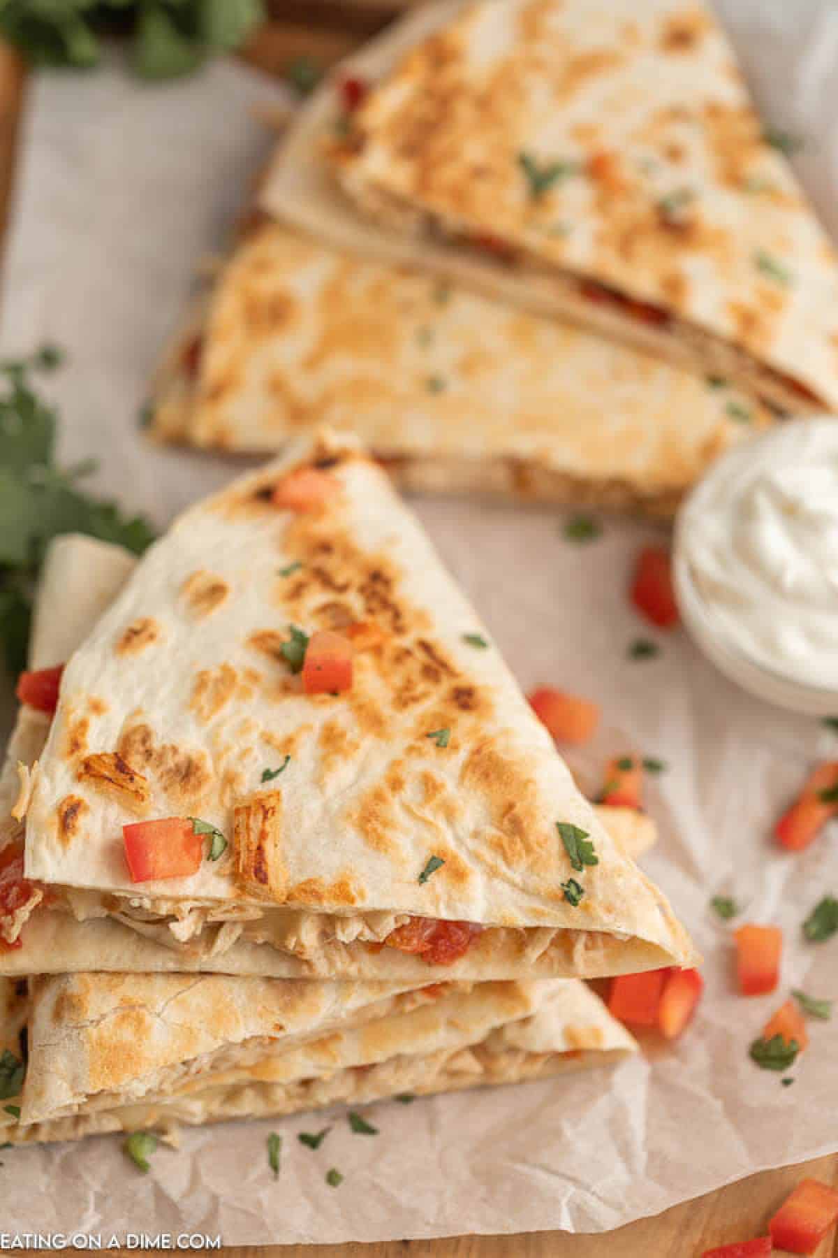 This crockpot chicken quesadilla recipe is so easy and packed with tons of flavor. Slow cooker chicken quesadilla recipe will be a new favorite. It's perfect for busy nights. Learn how to make chicken quesadillas. Close up image of chicken quesadilla's stacked with a side of sour cream.