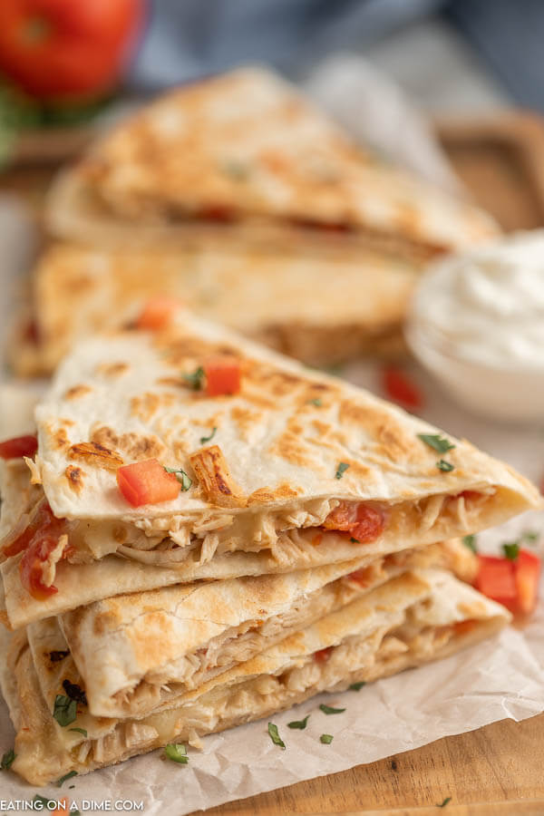 Close up image of chicken quesadilla's stacked with a side of sour cream. 