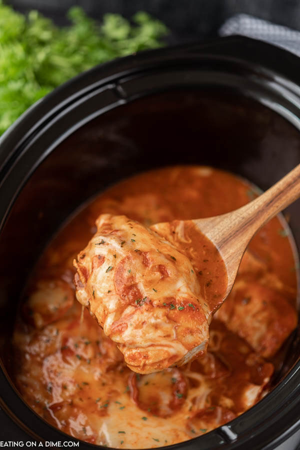 Close up image of pizza chicken in the crock pot with a serving on a wooden spoon. 