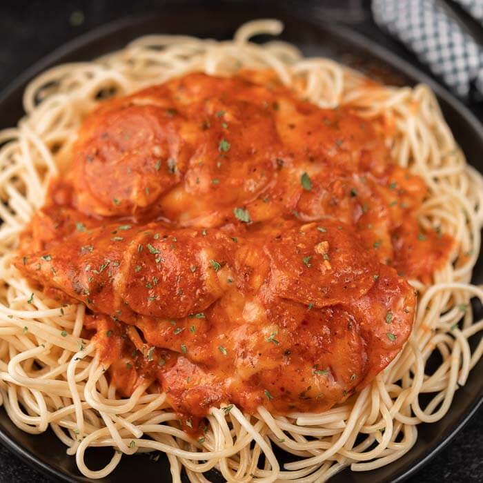 Close up image of pizza chicken on spaghetti on a black plate. 