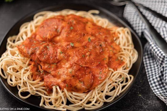 Close up image of pizza chicken on spaghetti on a black plate. 