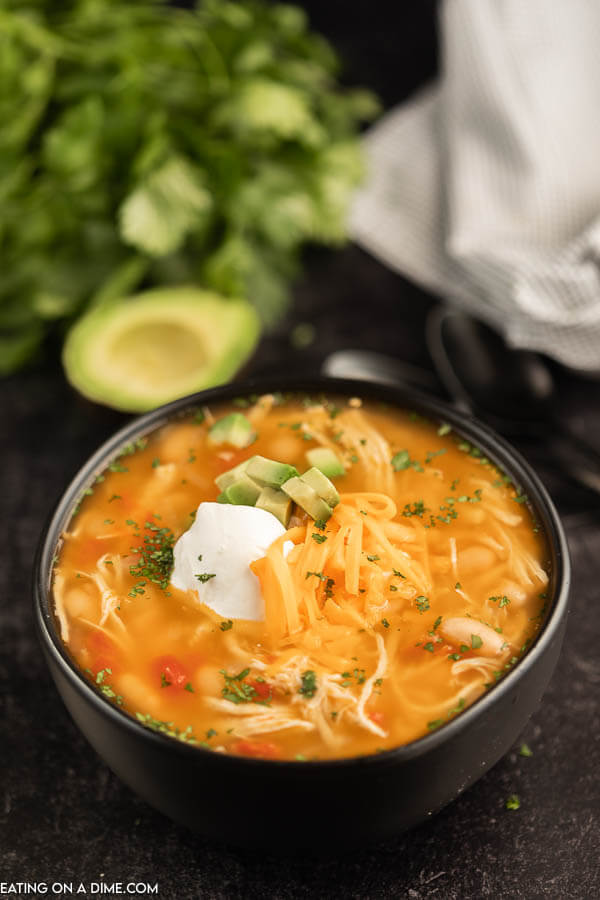 Close up image of chicken taco soup in a black bowl with avocado in the background. 