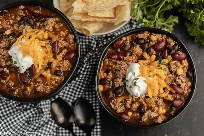 Close up image of two black bowls of taco soup with a side of tortilla chips and two spoons. 