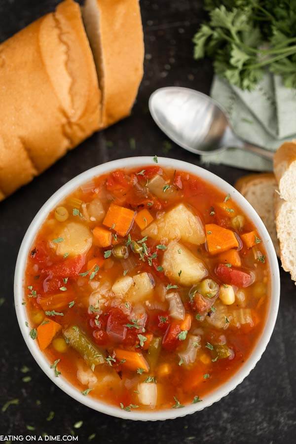 Close up image of vegetable soup in a white bowl with a side of french bread. 