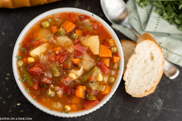 Close up image of vegetable soup in a white bowl with a side of french bread. 