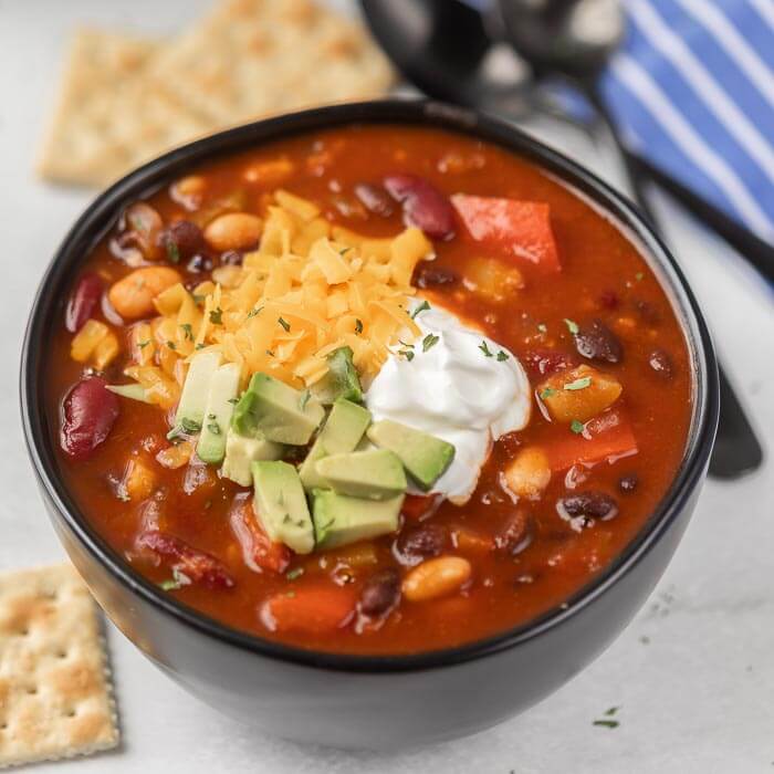 close up image of a bowl of vegetarian chili with crackers and spoons. 
