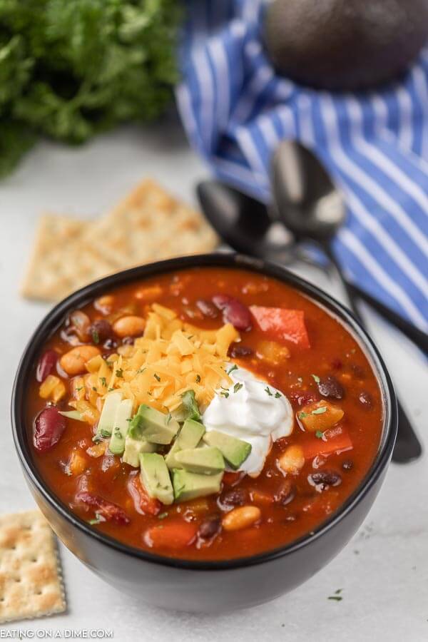 Close up image of a vegetarian chili in a black bowl with crackers and spoons. 