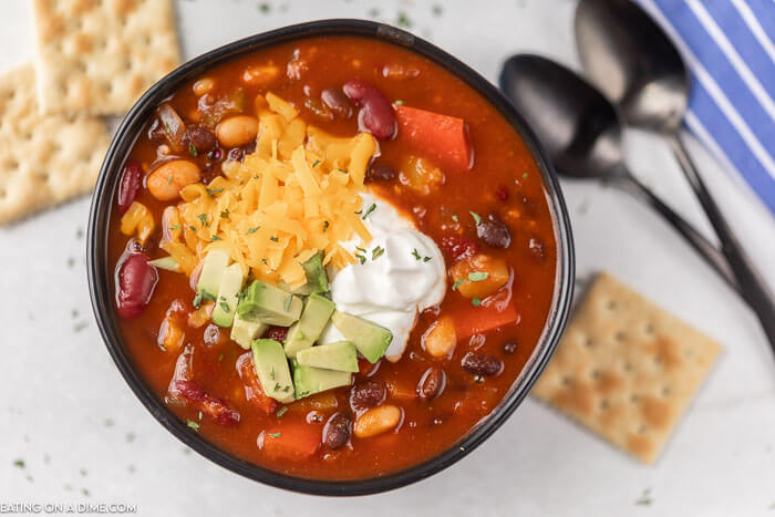 Close up image of vegetarian chili in a black bowl with crackers and two spoons. 