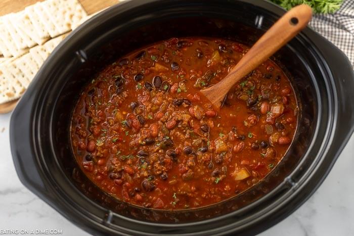 Close up image of vegetable and beef chili in a crock pot with a wooden spoon. 