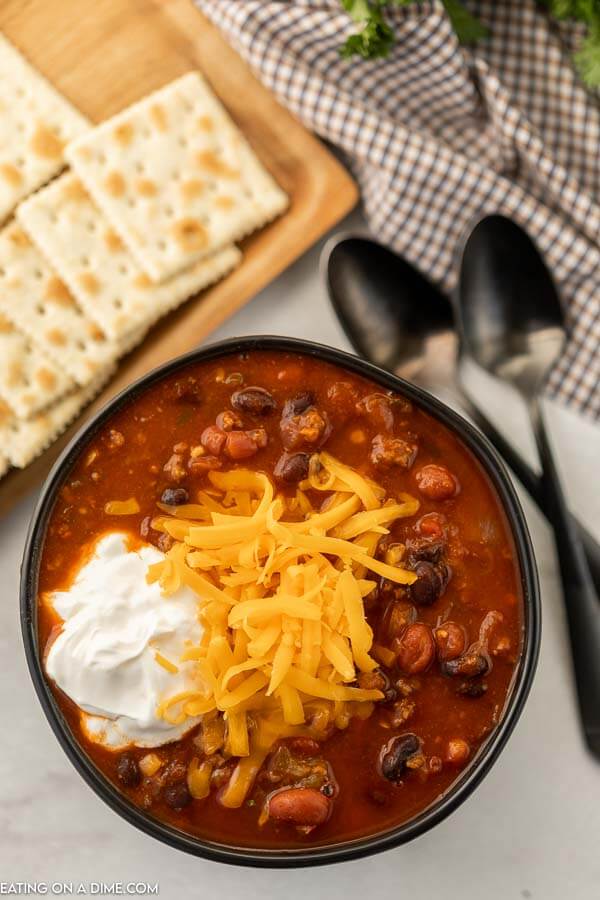 Close up image of a black bowl of vegetable and beef chili with a side of crackers. 