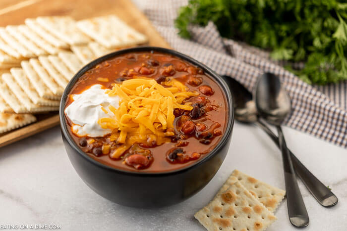 Close up image of a bowl of vegetable and beef chili with a side of crackers. 