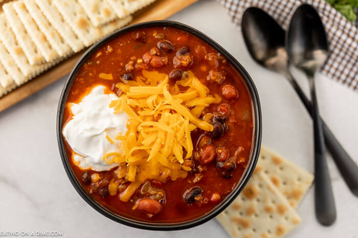 Close up image of a bowl of vegetable and beef chili with a side of crackers. 