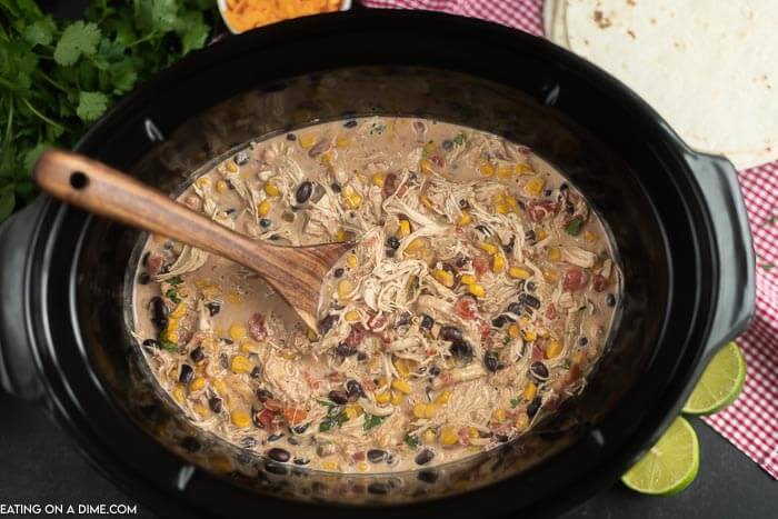 Close up image of fiesta chicken in the crock pot with a wooden spoon. 