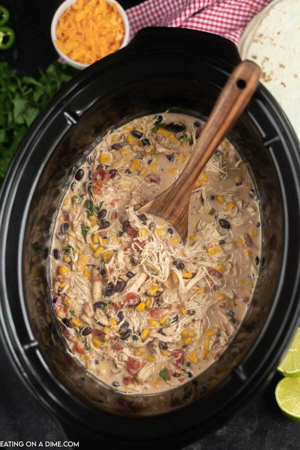 Close up image of fiesta chicken in the crock pot with a wooden spoon. 