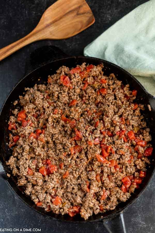 Close up image of ground beef being cooked in a iron skillet with a wooden spoon.