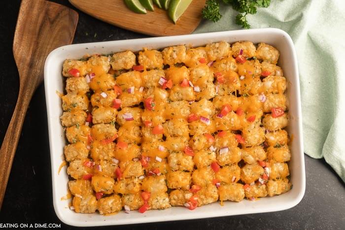Close up image of beef enchilada tator tot casserole topped with cheese and tomatoes in onions. 
