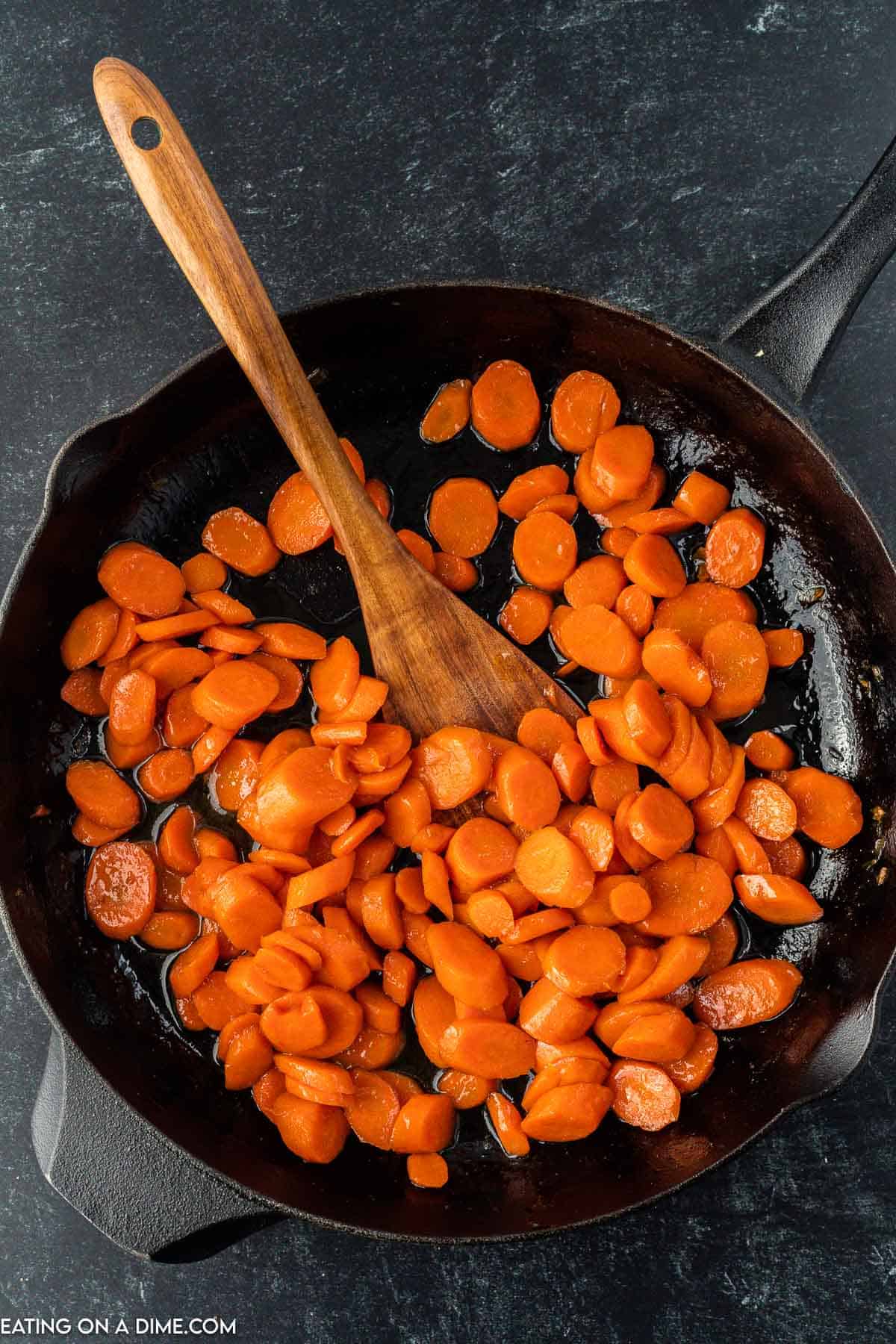 Combining carrots with brown sugar glaze in a skillet with a wooden spoon
