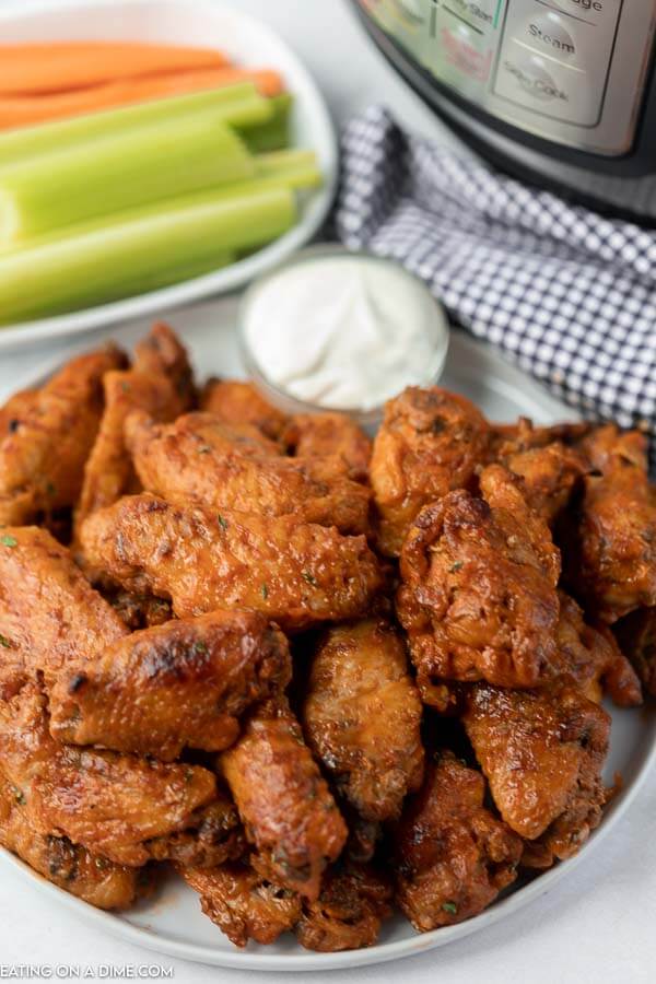 Close up image of chicken wings on a plate with a side of ranch. A plate of celery and carrots is also on the table. 