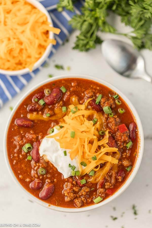 Close up image of a white bowl of chili topped with sour cream and cheese. 