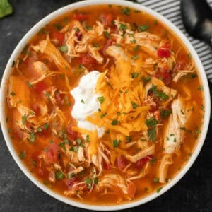 A bowl of Instant Pot chicken fajita soup topped with shredded cheese, a dollop of sour cream, and chopped cilantro, placed next to a spoon and a striped napkin.