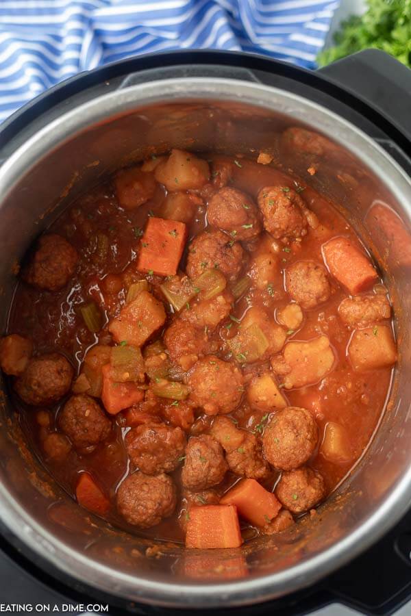 Close up image of a white bowl of meatball stew with a side of crackers. 