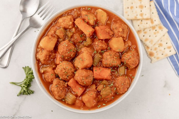 Close up image of a white bowl of meatball stew with a side of crackers. 