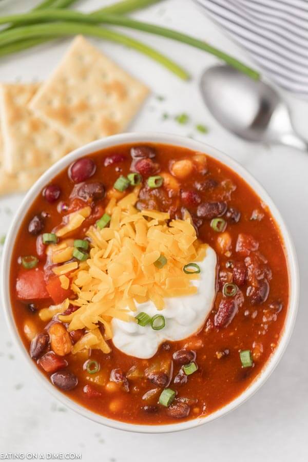 Close up image of vegetarian chili in a white bowl topped with sour cream and cheese. 