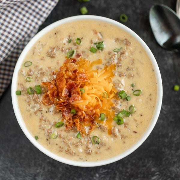 Close up image of a bowl of cheeseburger soup topped with chives, bacon, and cheese 