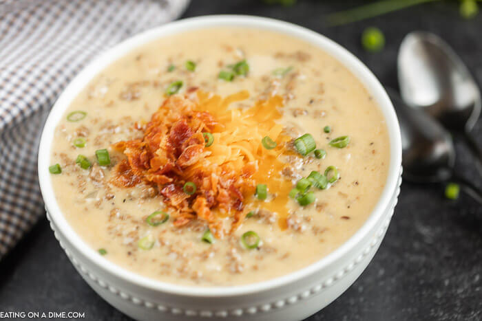 Close up image of a bowl of cheeseburger soup topped with chives, bacon, and cheese 