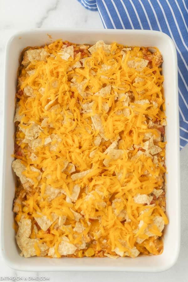 Chicken mixture in baking dish with shredded cheese and tortilla chips. 