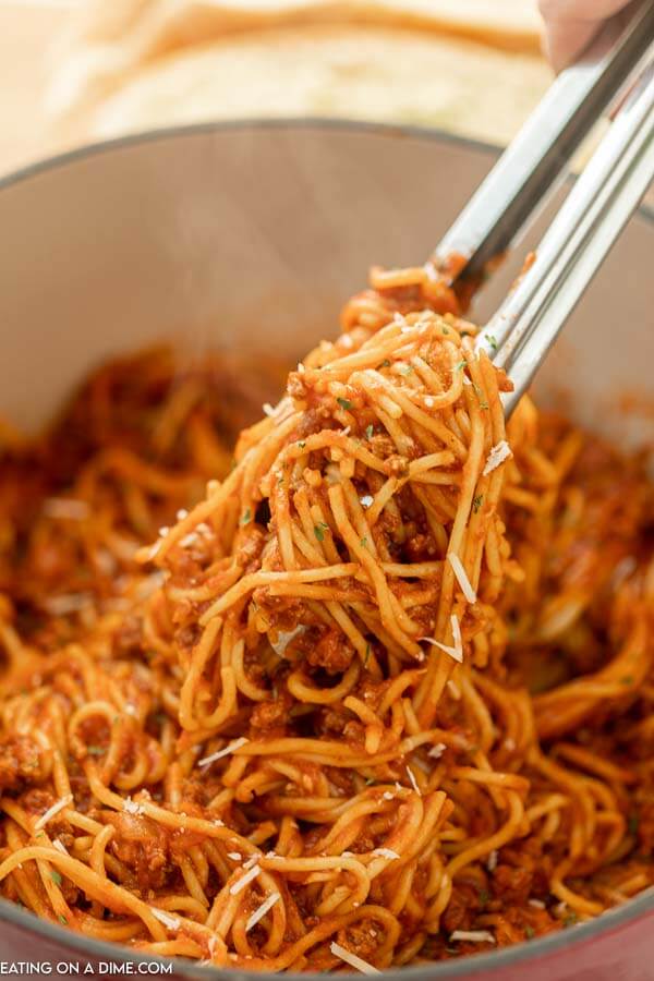 Close up image of a pot of spaghetti with a serving on silver tongs. 