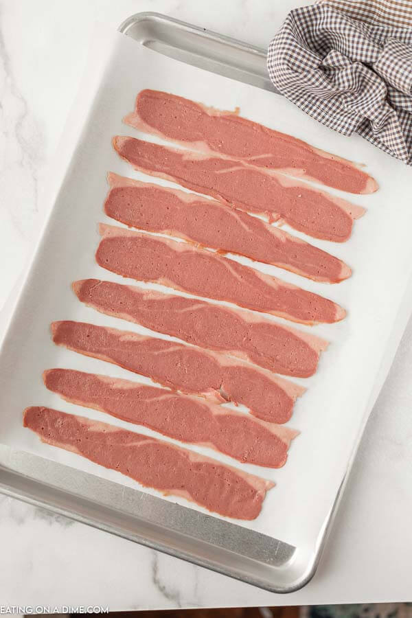 Close up image of uncooked turkey bacon on a baking sheet. 
