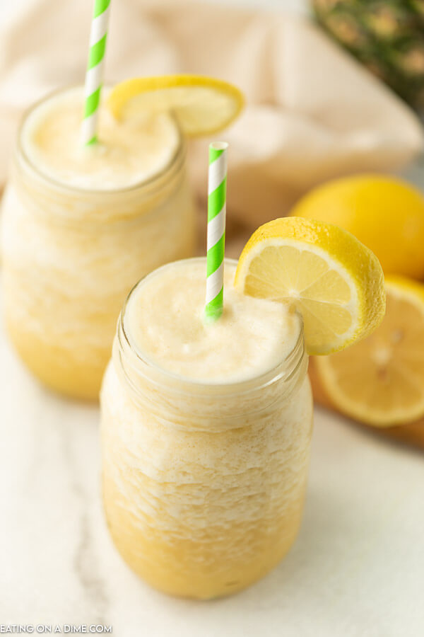 Close up image of pineapple lemonade slushie in a mason jar with a lemon and a straw.