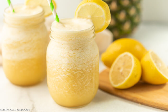Close up image of pineapple lemonade slushie in a mason jar with a lemon and a straw.