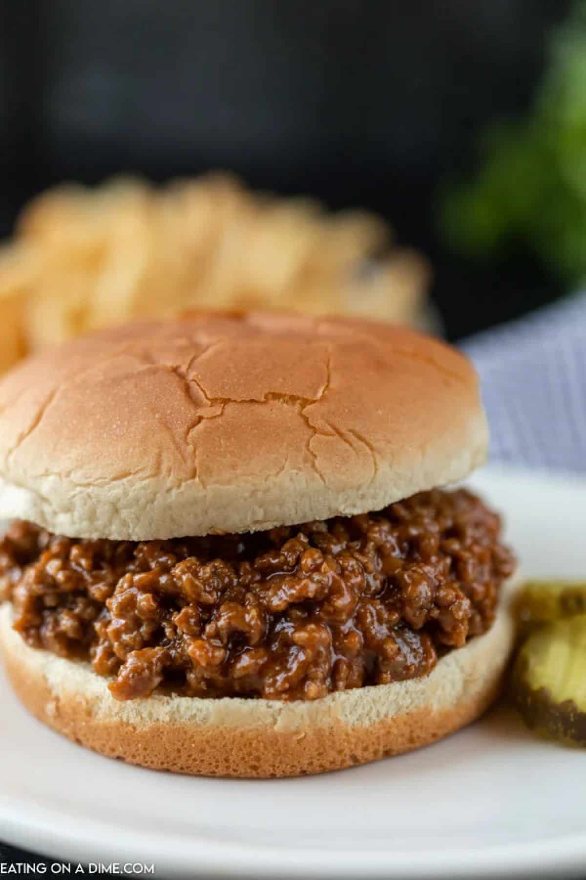 Close up image a sloppy joes on a bun with pickles on the side. 
