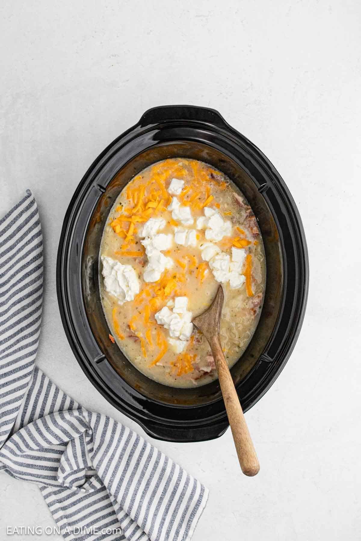 Cream cheese and shredded cheese added to the crockpot with the creamy mixture.