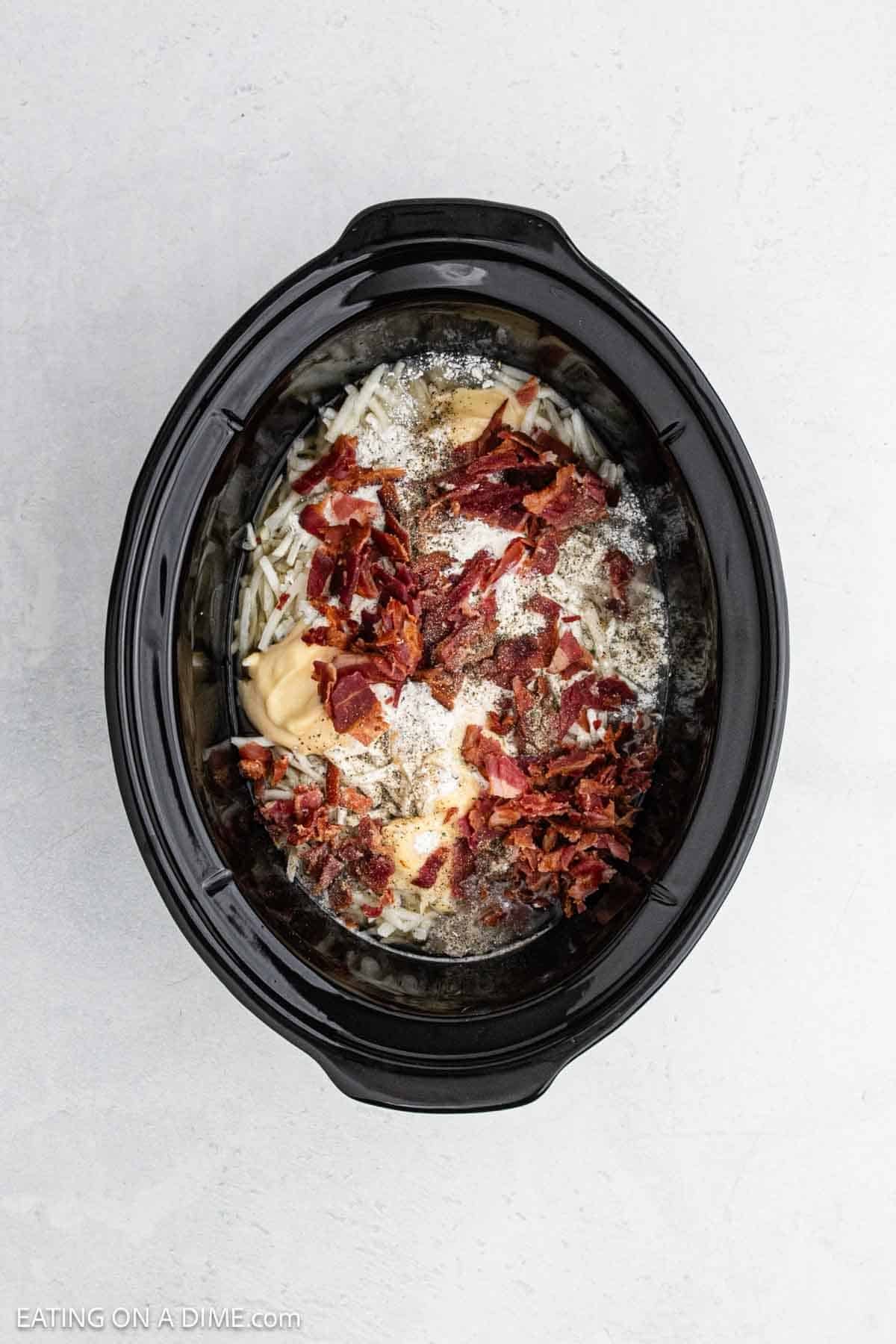 Crispy bacon, shredded hashbrowns, spices, and broth added to the slow cooker.