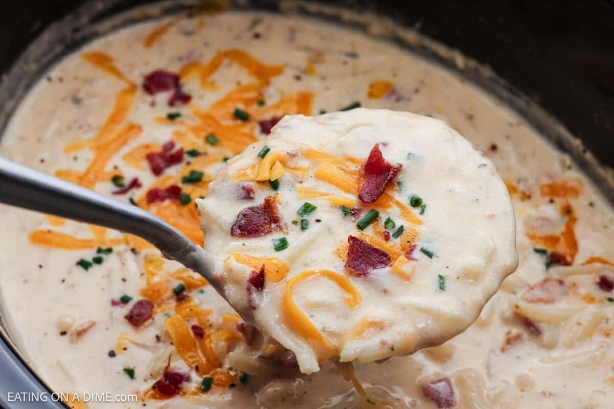 A serving of Crack Potato Soup in a ladle over the soup in the crockpot.