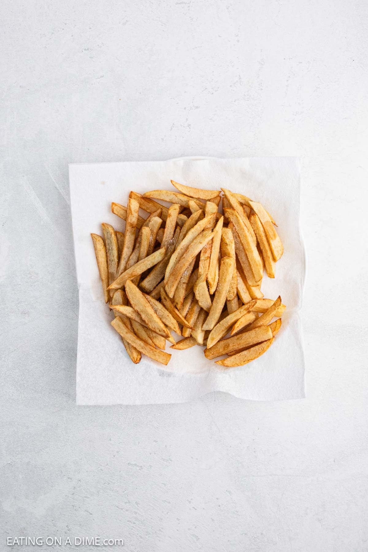 A pile of golden-brown French fries sits on a white paper towel.