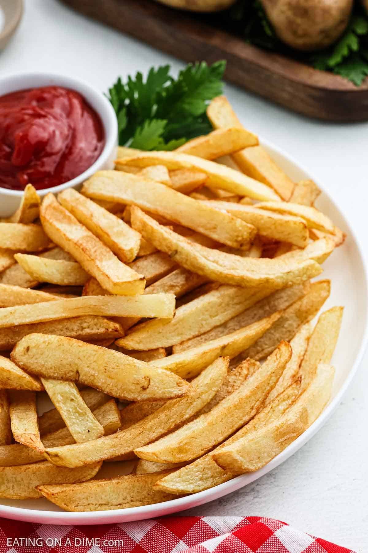 A plate of golden, crispy French fries is served with a small bowl of ketchup, garnished with fresh parsley.