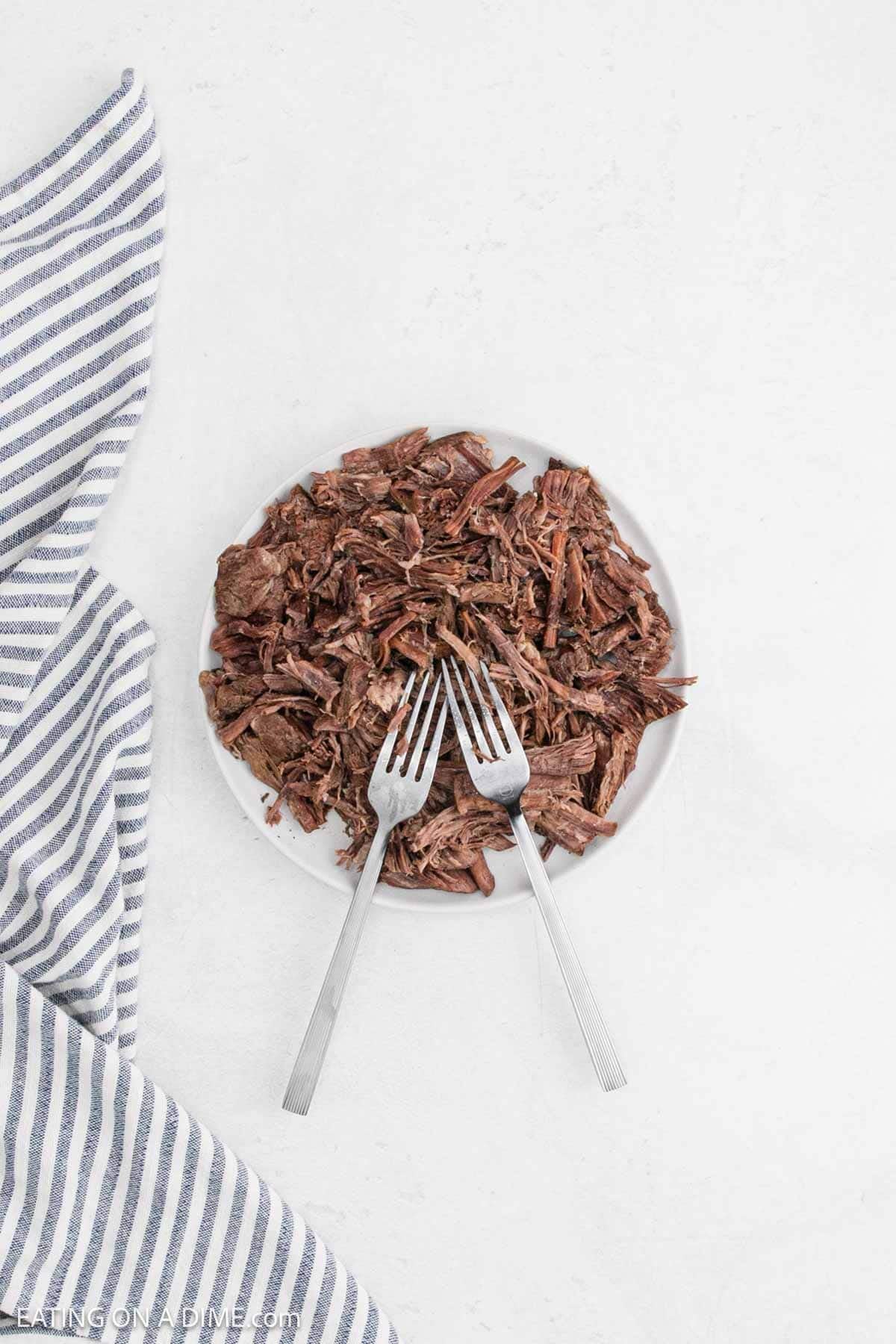 Shredding the cooked roast on a plate with two forks.